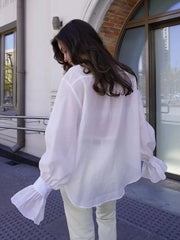 Person wearing a white blouse with ruffled sleeves in front of a building.