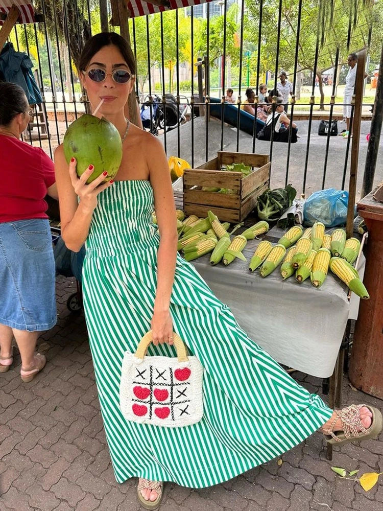 Woman in a green and white striped dress holding a coconuts at an outdoor market.