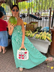 Woman in a green and white striped dress holding a coconuts at an outdoor market.