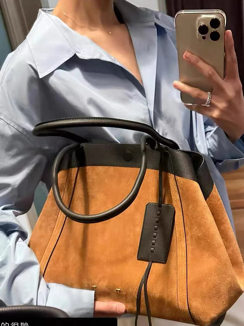 Person holding a brown leather handbag with a visible brand tag, wearing a light blue shirt.
