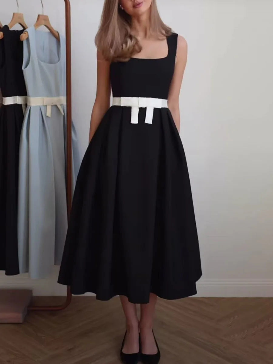Woman wearing a black dress with a white belt standing in front of a rack of dresses.