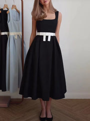 Woman wearing a black dress with a white belt standing in front of a rack of dresses.