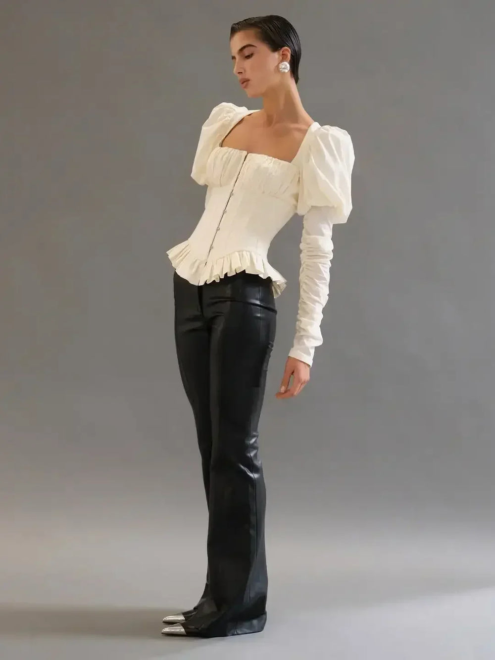 Woman wearing a white blouse with puffed sleeves and black leather pants against a gray background