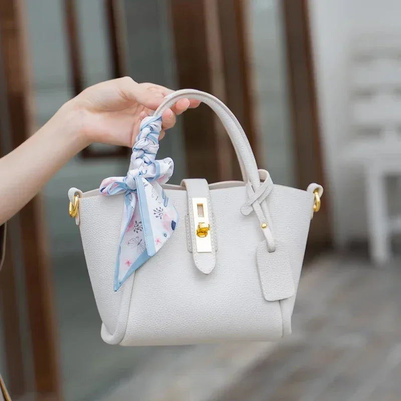 White handbag with a decorative ribbon held by a hand against a blurred indoor background
