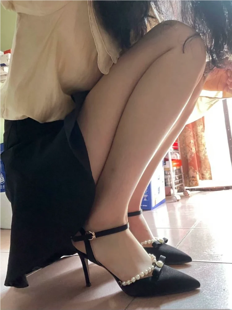 Person wearing black high-heeled shoes with pearl details in a room.