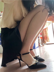 Person wearing black high-heeled shoes with pearl details in a room.