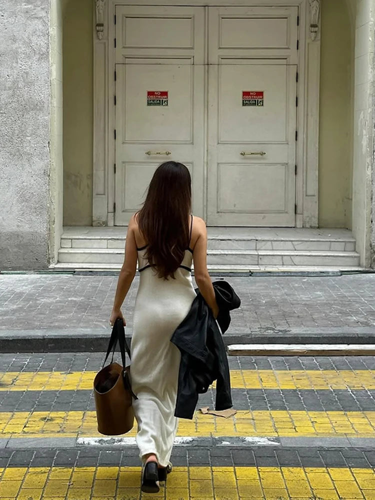 Woman walking on a street with a white dress and brown bag