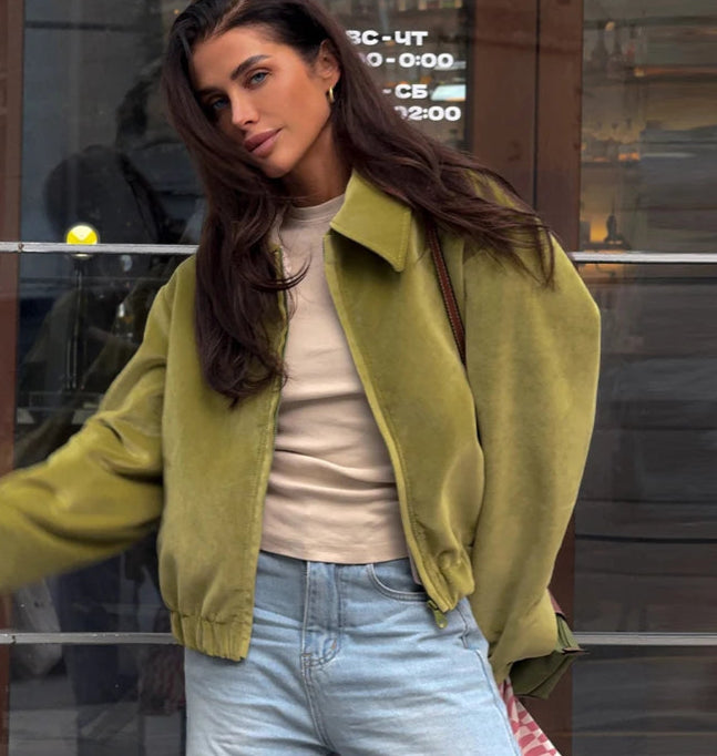 A woman wearing a green jacket and light blue jeans in front of a Club window.