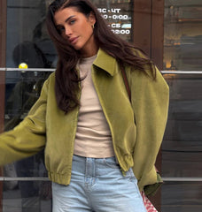 A woman wearing a green jacket and light blue jeans in front of a Club window.