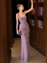Woman in a purple beaded evening gown standing in front of a bookshelf.