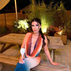 Woman sitting on a wooden bench outdoors with plants and lights in the background