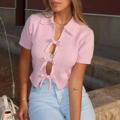 Woman wearing a pink ribbed top with a tie detail and light blue jeans, sitting on steps.