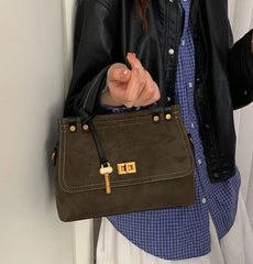 Person holding a brown leather handbag with a gold clasp against a neutral background