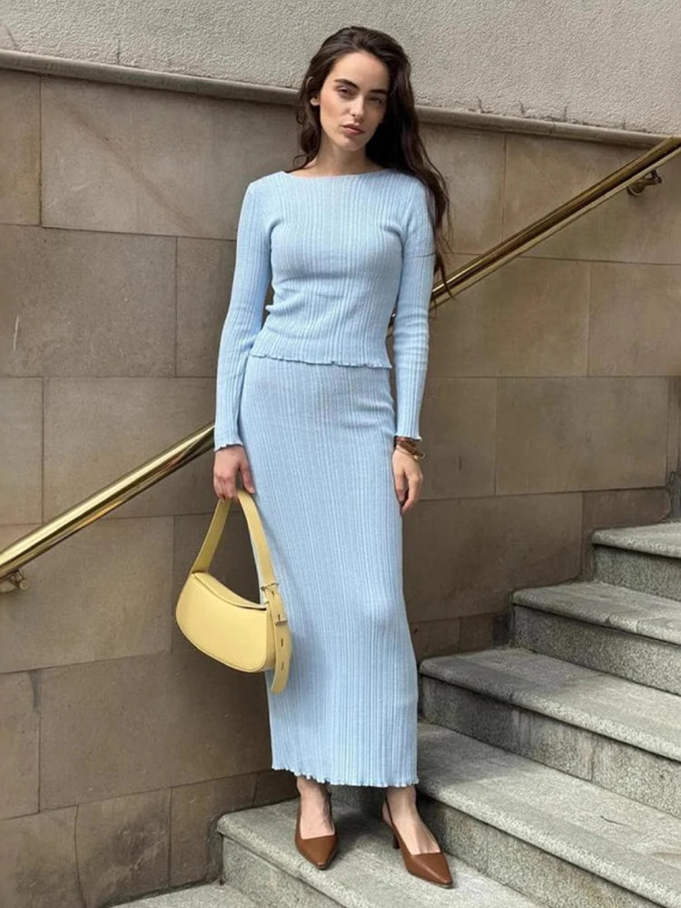 Woman in a light blue outfit standing on stone steps with a beige handbag.