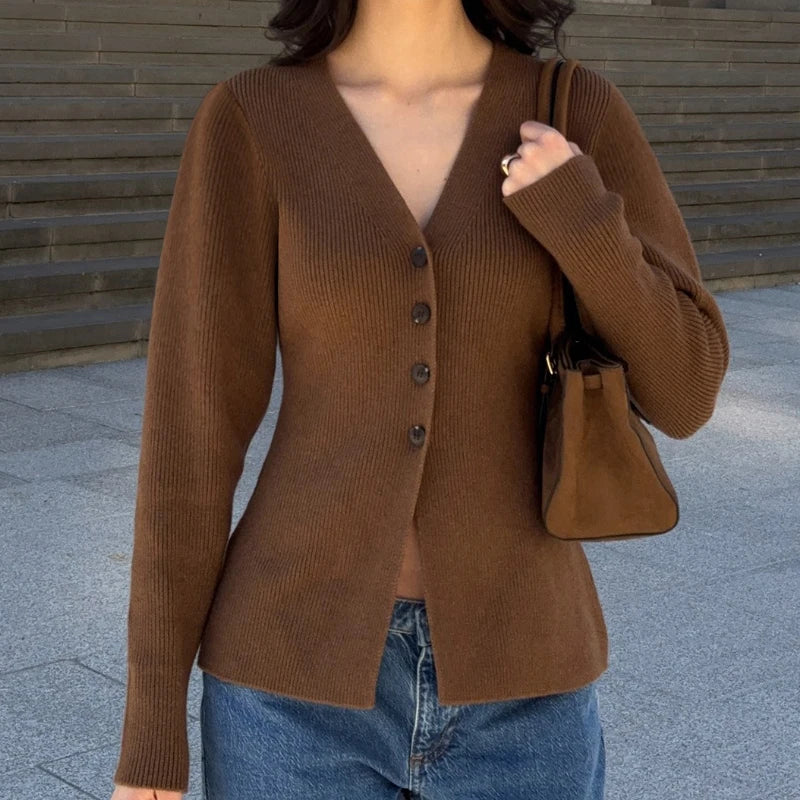 Person wearing a brown cardigan and holding a brown handbag against a wooden wall background