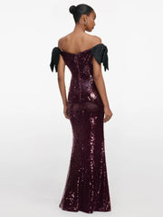 Woman wearing a burgundy sequin gown with black bow straps on a white background