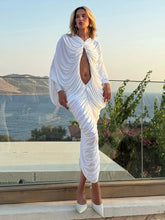 Woman in a white dress standing by a glass railing with a scenic view of water and mountains.