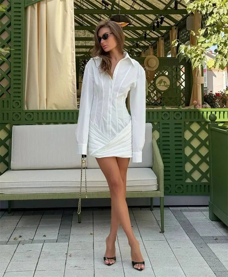 Woman in a white outfit standing in an outdoor setting with green lattice and white bench.