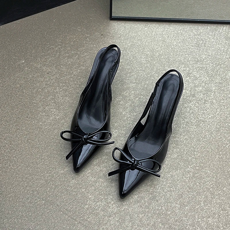 Black high-heeled shoes with bow details on a gray surface