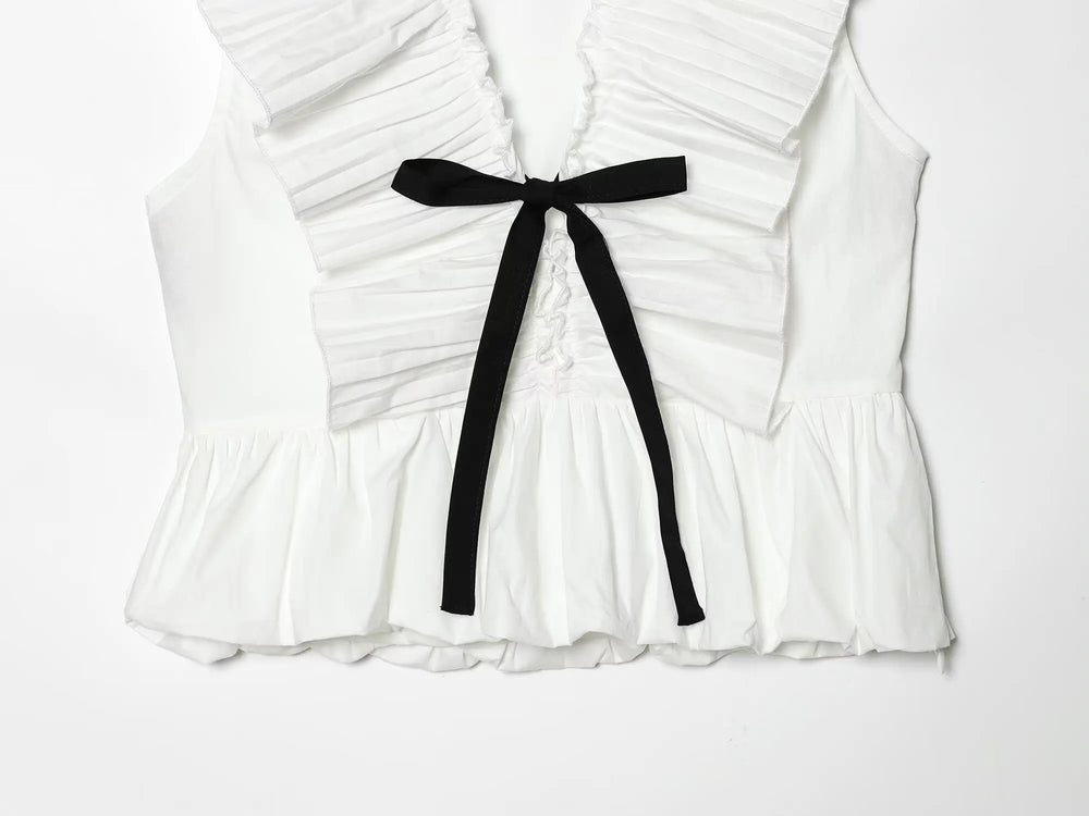 Close-up of the bow tie and pleated details on a white sleeveless peplum top.
