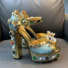Decorative high-heeled shoes with gold, blue, and pearl details on a gray surface.