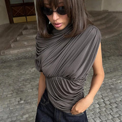 Person wearing a gray draped top and sunglasses on a stone pavement.