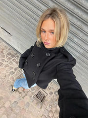 Person wearing a black coat taking a selfie on a street.