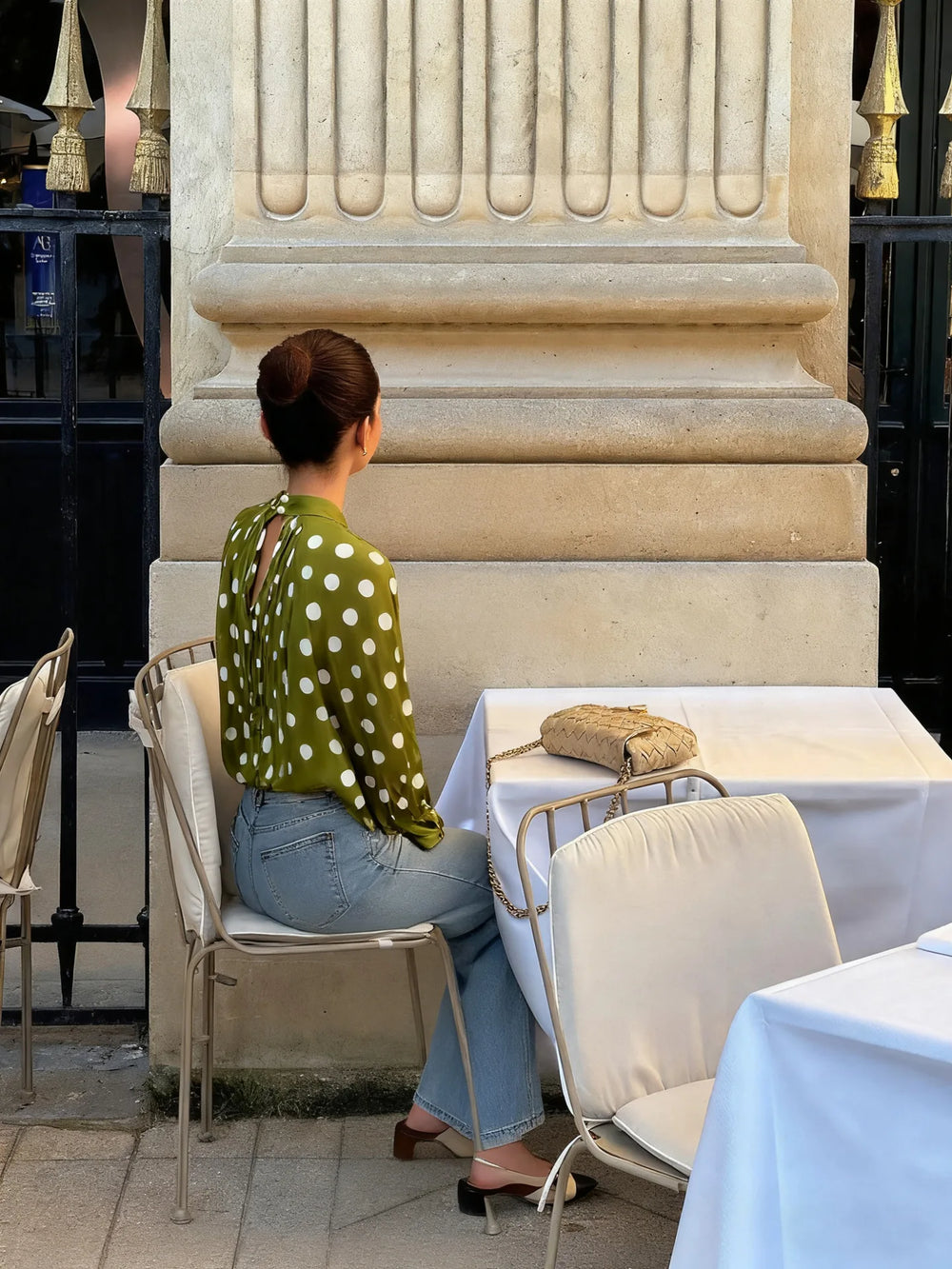 Woman sitting at a table in an elegant outdoor setting with classical architecture.