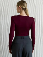 Person wearing a burgundy long-sleeve top and dark pants against a neutral background