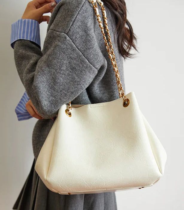 Person holding a white handbag with gold chain strap against a neutral background