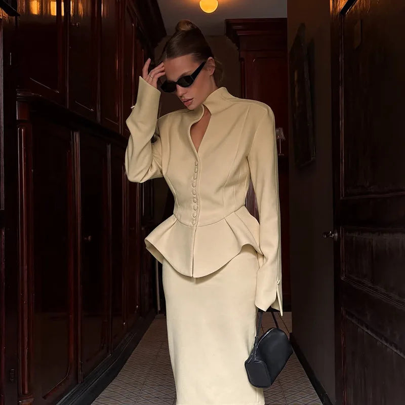 Woman in a beige peplum top and skirt walking through a hallway.