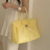 Yellow structured tote bag with lock detail carried by a person.
