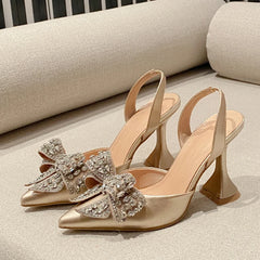 Gold high-heeled shoes with decorative bows on a light background