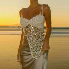 Woman wearing a crochet top with sequin embellishments on a beach at sunset.