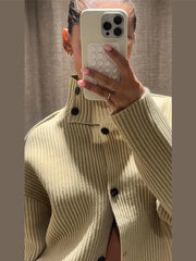 Person wearing a beige ribbed sweater with black buttons, holding a phone with a white case.