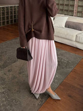 Person wearing a brown sweater and pink pleated skirt in a living room.