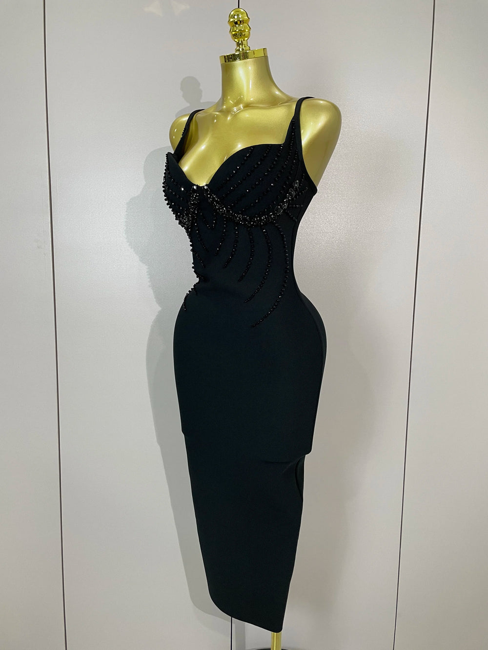 Black dress with bead detailing on a mannequin against a white background