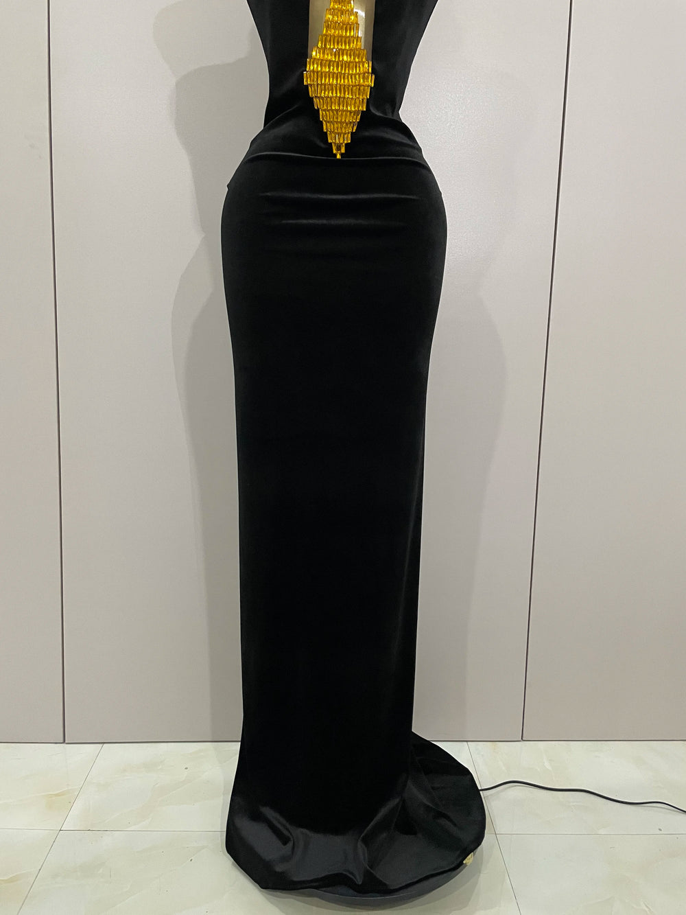 Black evening gown with gold embellishments on a mannequin against a white background