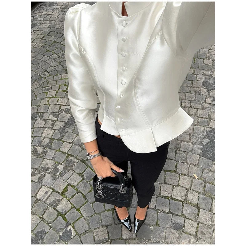 Person wearing a white satin blouse and black pants on a cobblestone street.