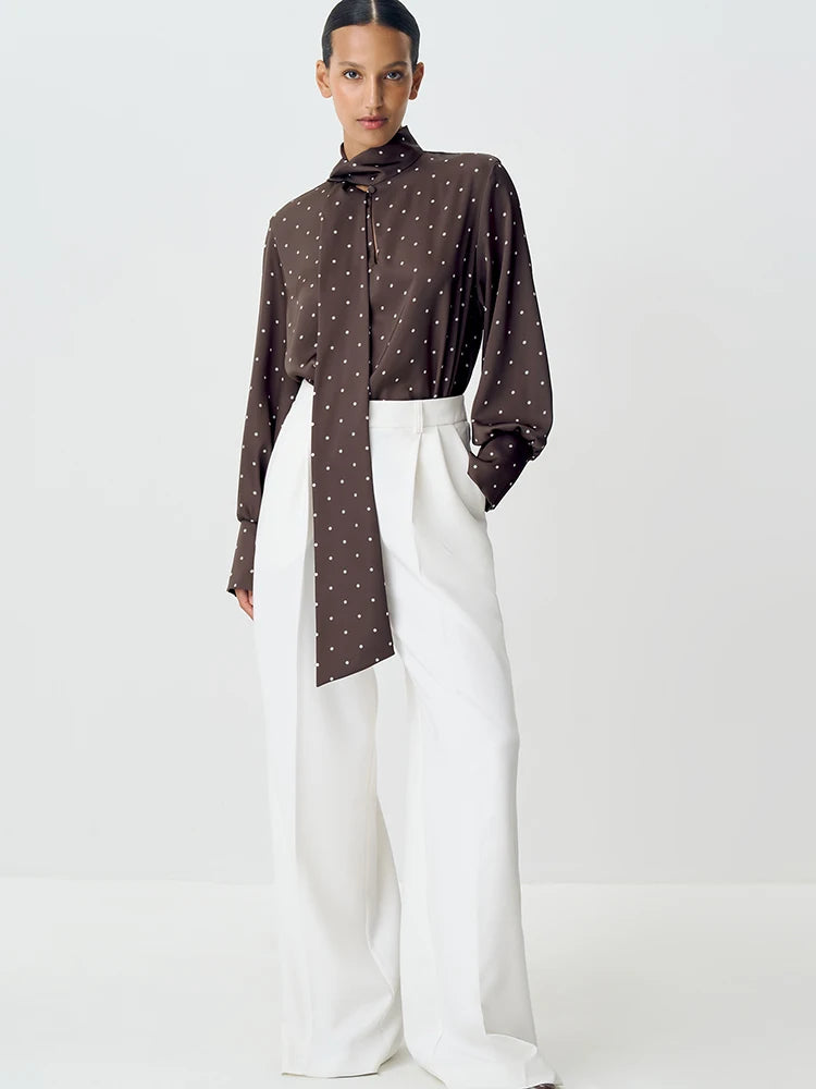 Woman wearing a brown polka dot shirt and white pants on a white background