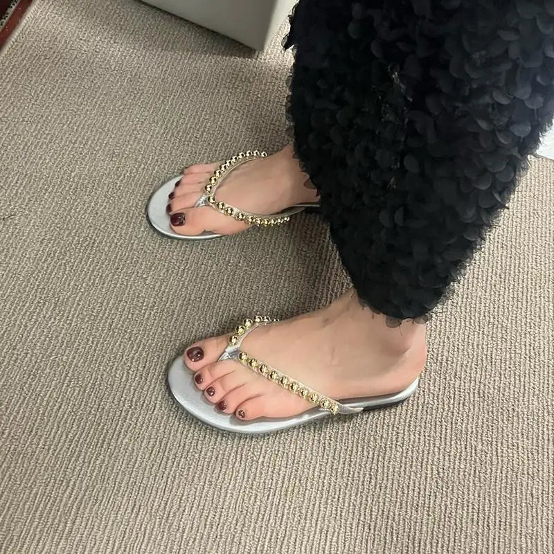 Feet wearing silver flat embellished flip flops.