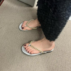 Feet wearing silver flat embellished flip flops.