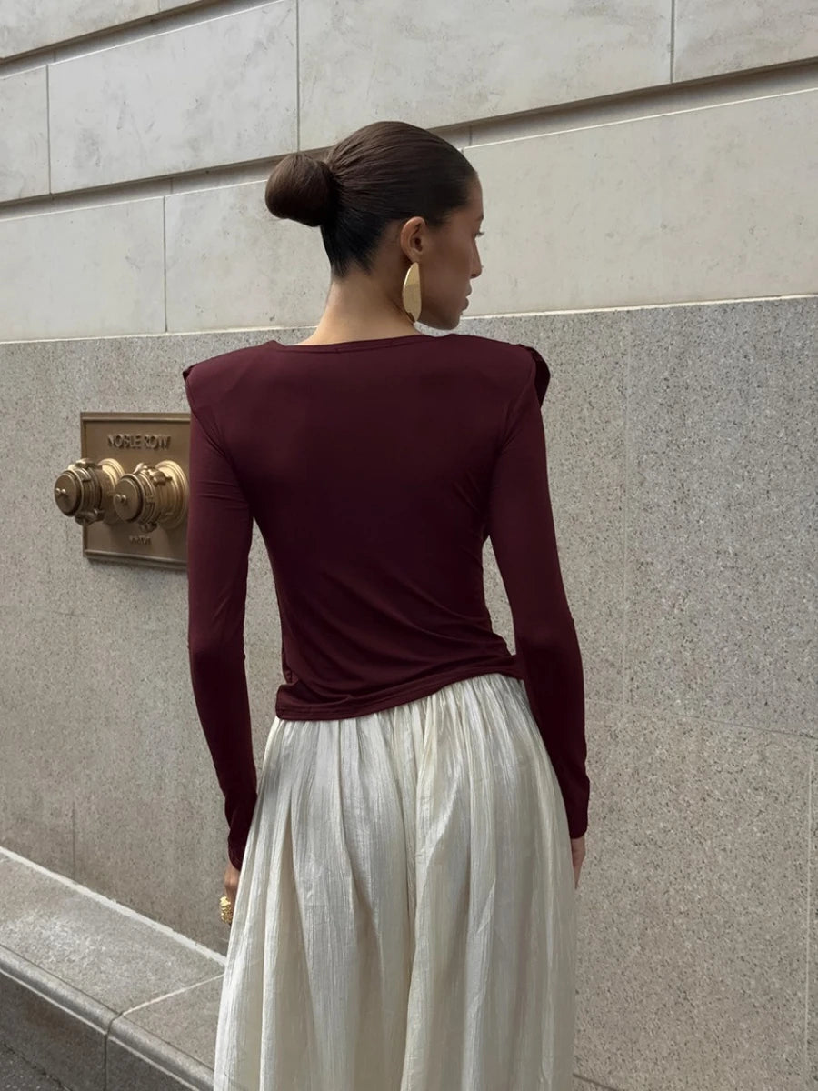 Woman wearing a burgundy top and white skirt against a stone wall.