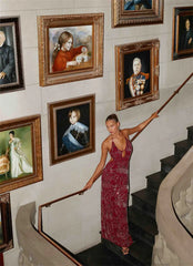 Woman in a red dress standing on a staircase with portraits on the wall