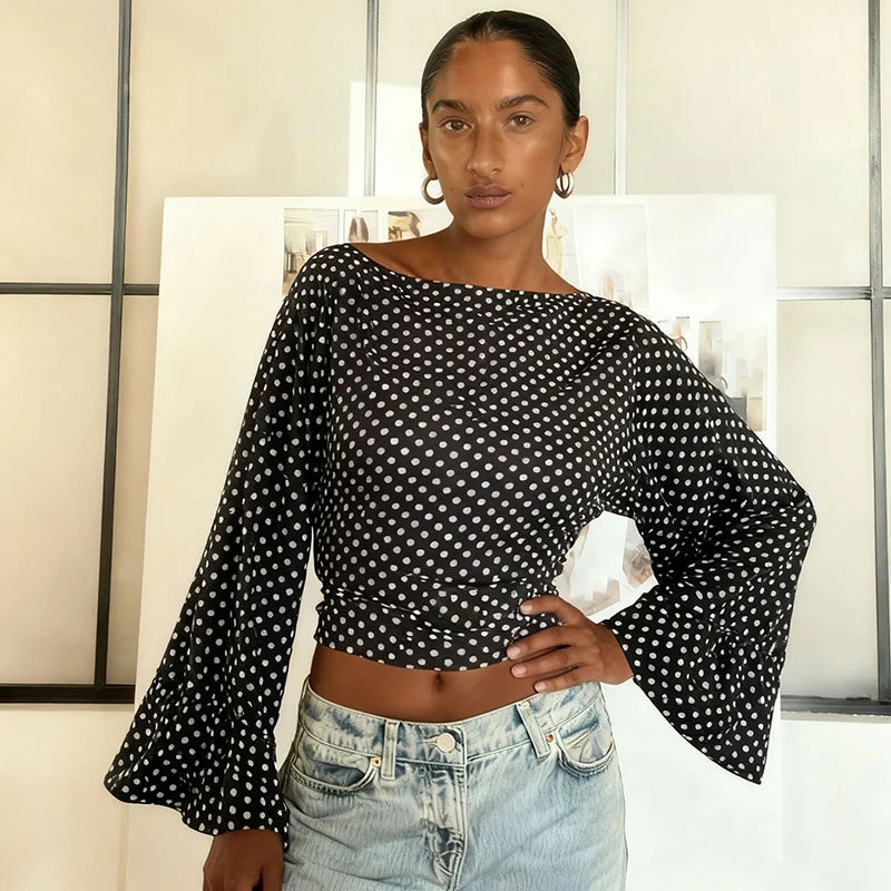 Woman wearing a black polka dot blouse with long sleeves and light blue jeans indoors.
