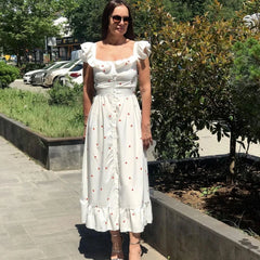 Woman in a white dress with ruffled sleeves and hem standing outdoors.