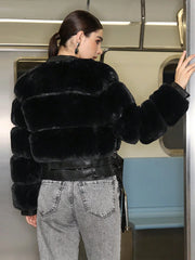 Person wearing a black fur coat and gray jeans on a subway train.