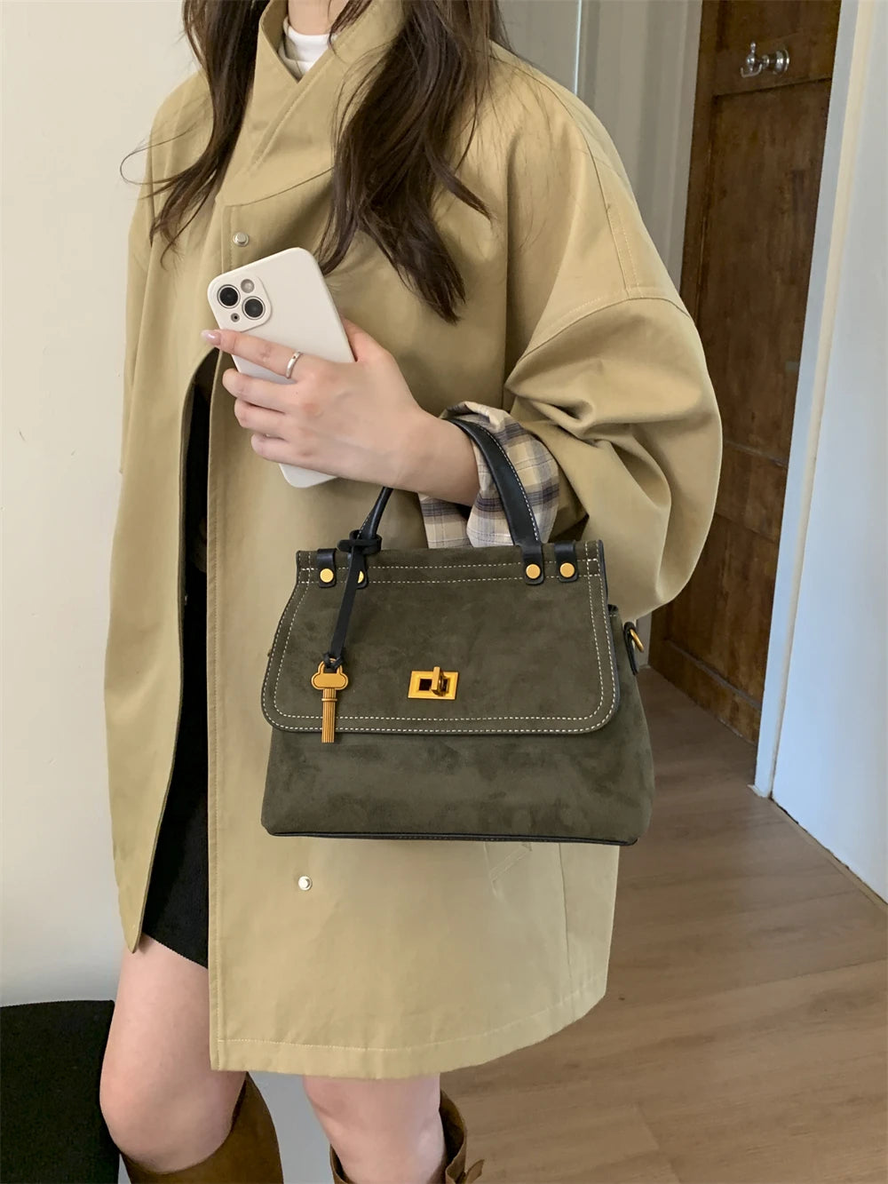 Person holding a green handbag with a gold clasp indoors.
