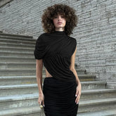 Woman in a black dress standing on stone steps with a stone wall background