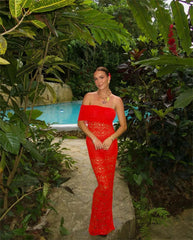 Woman in a red dress standing in a tropical setting with a pool and lush greenery.